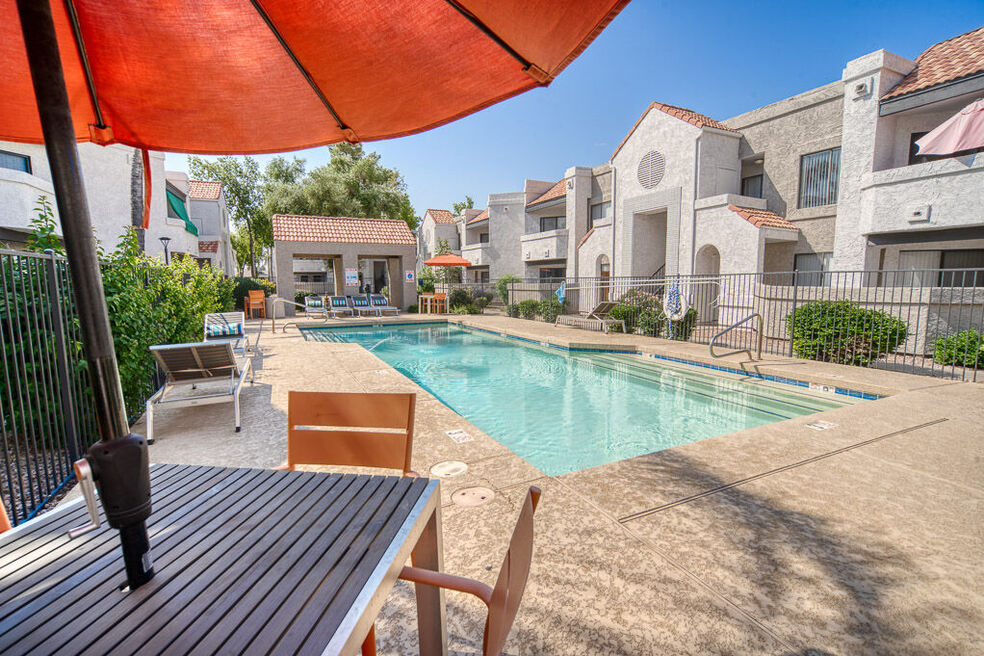 inside the pool area with a table and a retractable umbrella for the tables