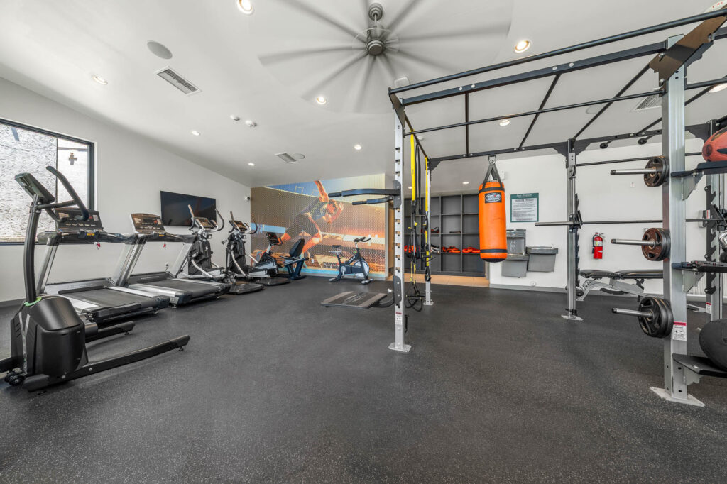 fitness center with various cardio and strength building equipment with a large ceiling fan and storage shelves