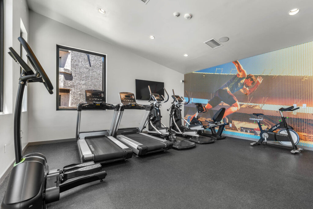 fitness center with various cardio training equipment, mounted television on the wall, and a fitness mural
