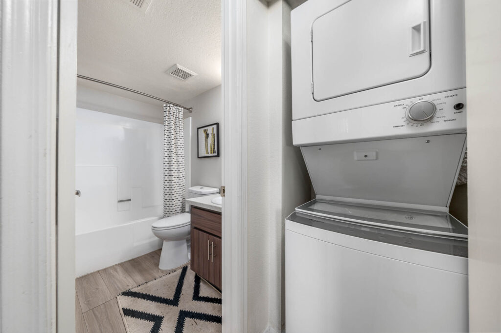 washer and dryer unit in closet space with view of adjacent bathroom